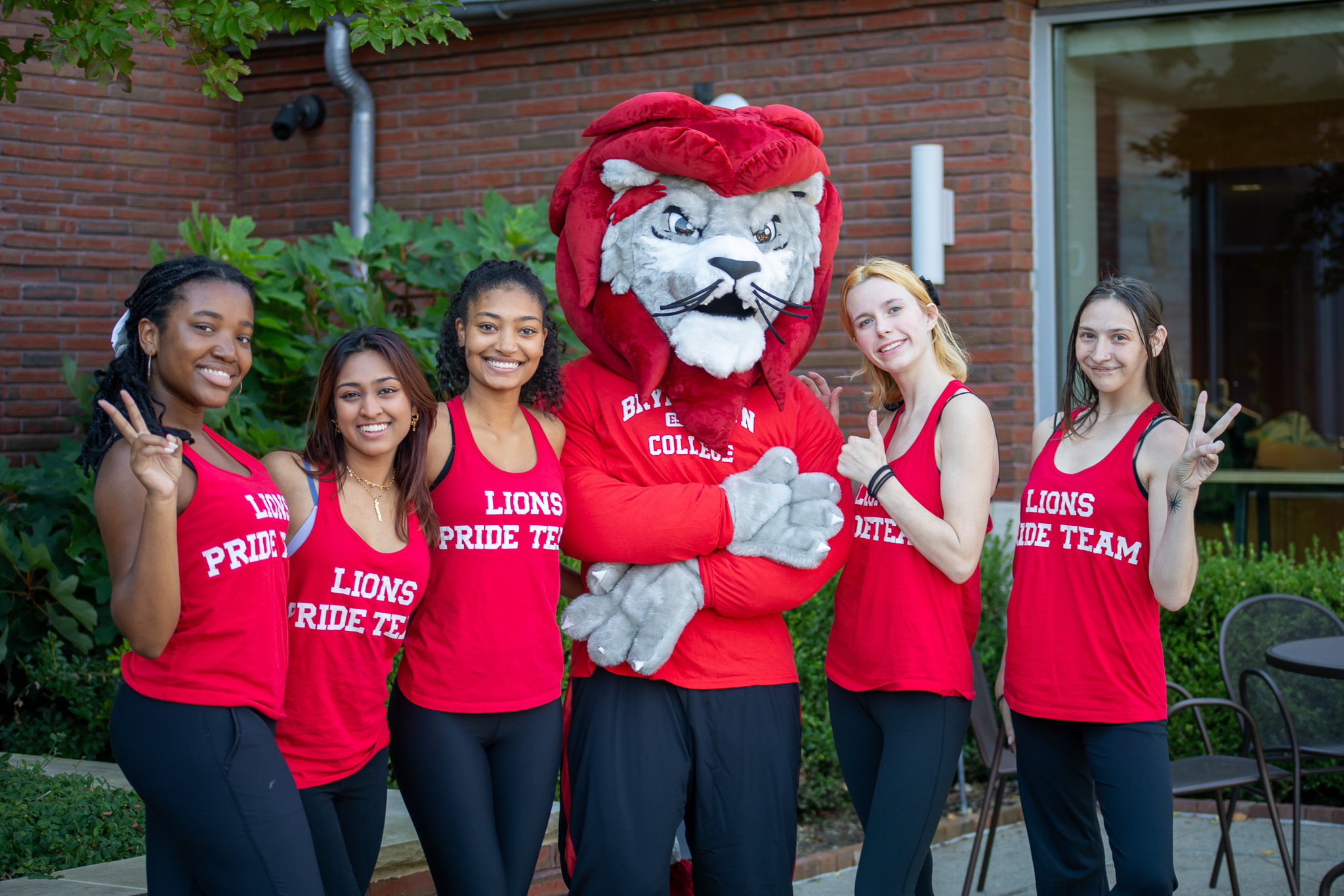 Leo the Lion mascot stands with two students in the residence courtyard