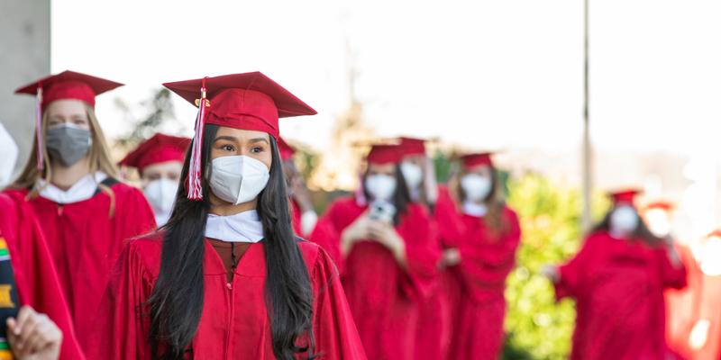 Class of 2020 students wear masks along with their traditional red cap and gown