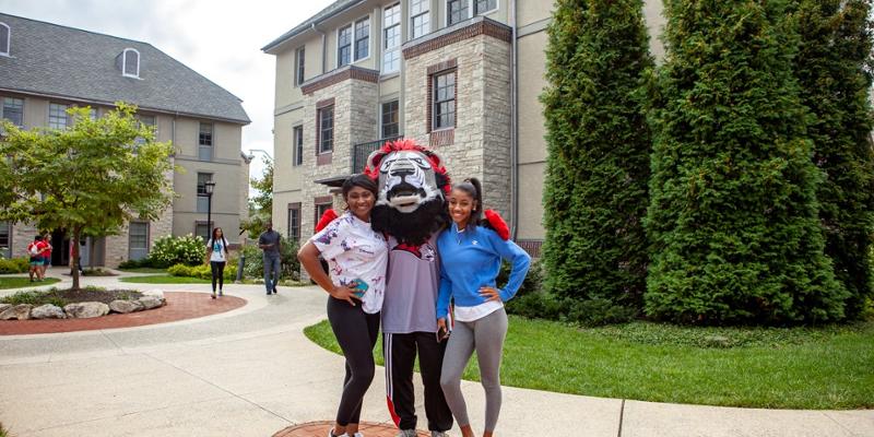 Leo the Lion mascot stands with two students in the residence courtyard