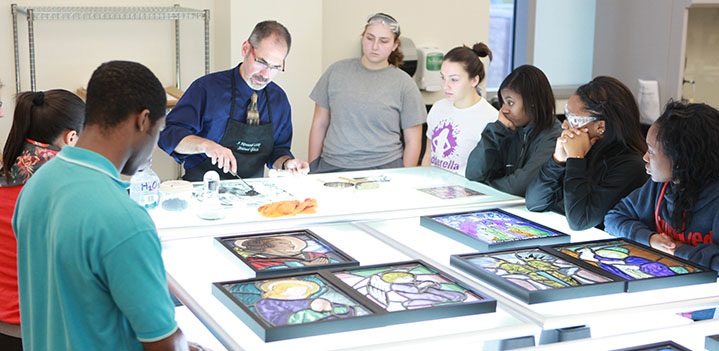 Professor shows students how to work with stained glass on a lit table