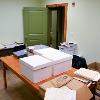 Boxes, folders, and documents are stacked on the table and along the walls of the archive